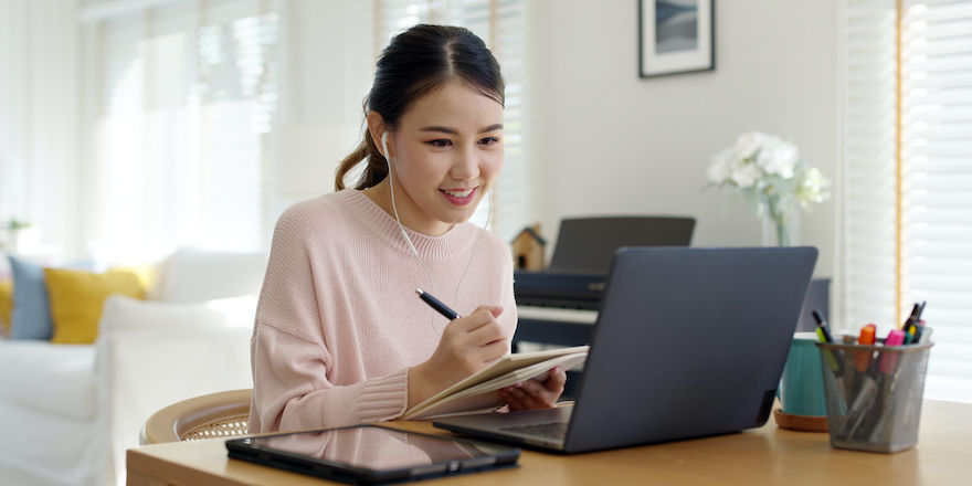 Candid young attractive asian female employee wear earphone listen to digital online course development program in quarantine social distance at home reskill upskill school class for career path.